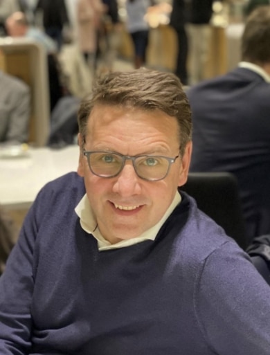 Mann mit Brille lächelt am Tisch, repräsentiert die positive Teamkultur von Unsere Grüne Glasfaser.