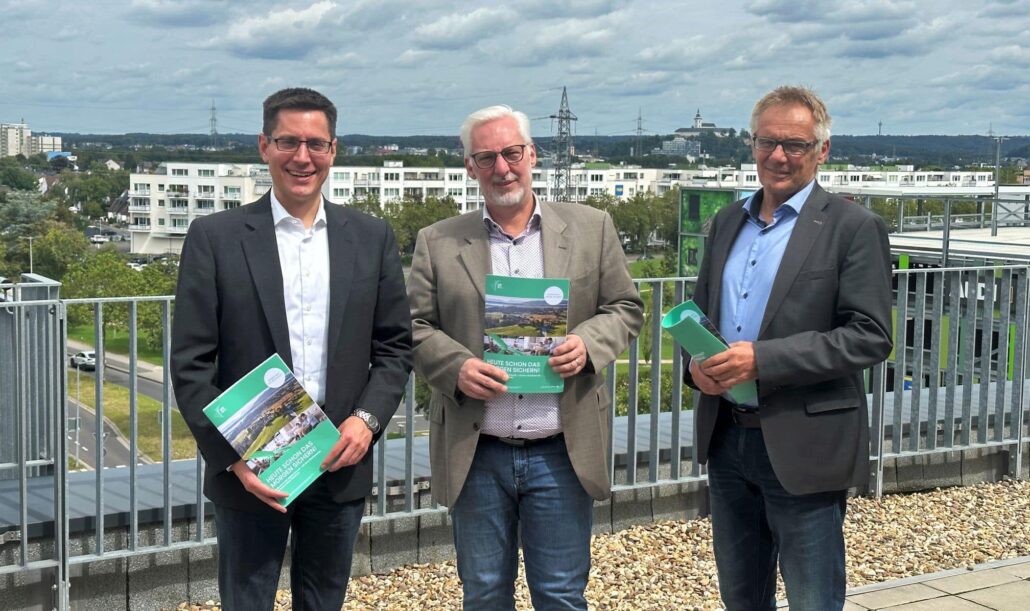 Drei Vertreter von Unsere Grüne Glasfaser präsentieren neue Informationsmaterialien auf einem Dach mit Ausblick.