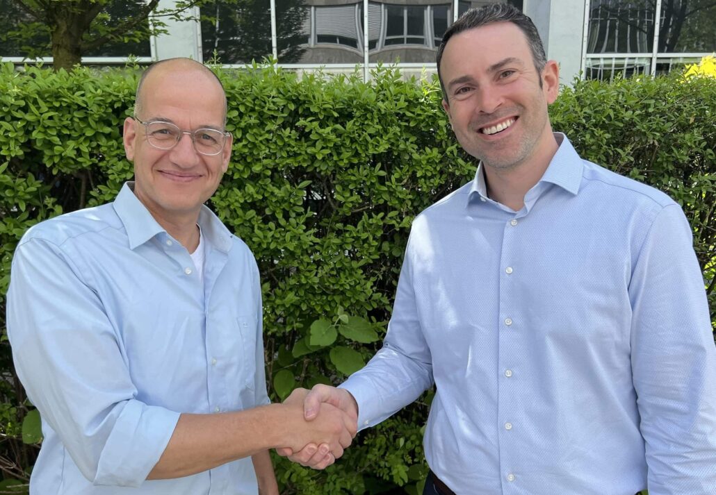 Zwei Männer schütteln sich die Hände vor einer grünen Hecke, Symbol für Partnerschaft bei Unsere Grüne Glasfaser.