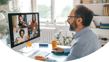 Mann arbeitet an einem Computer und führt ein Video-Meeting mit mehreren Teilnehmern, symbolisiert digitale Vernetzung.