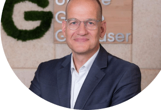 Portrait eines Mitarbeiters von Unsere Grüne Glasfaser vor dem Firmenlogo, das die nachhaltige Internetversorgung repräsentiert.