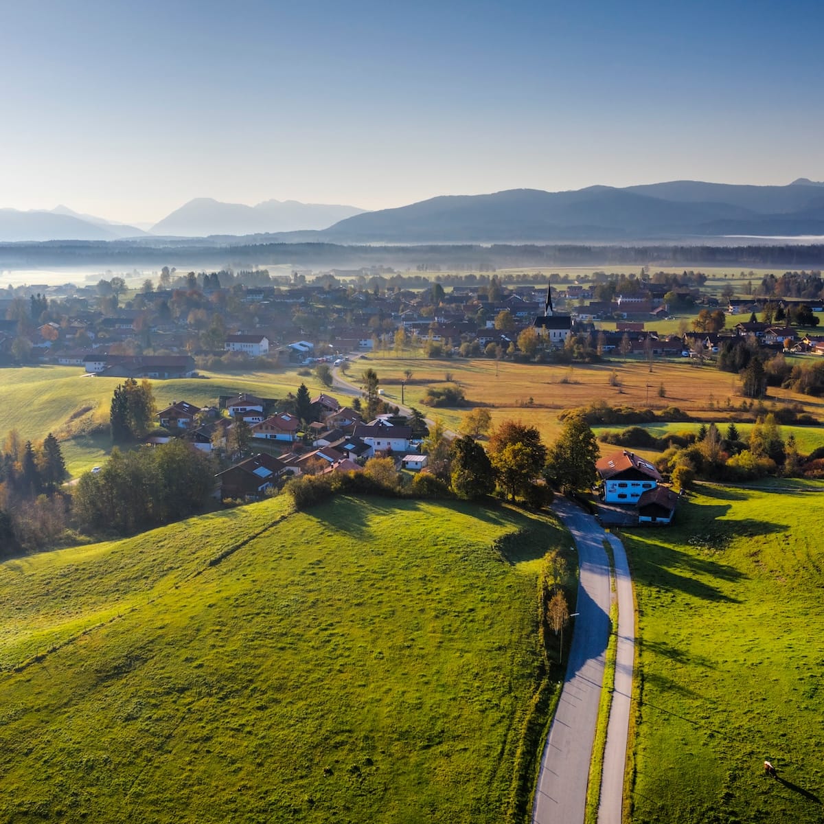 Landschaft mit grünen Wiesen und einem Dorf im Hintergrund, ideal für den Ausbau von Glasfaserinternet in ländlichen Regionen.