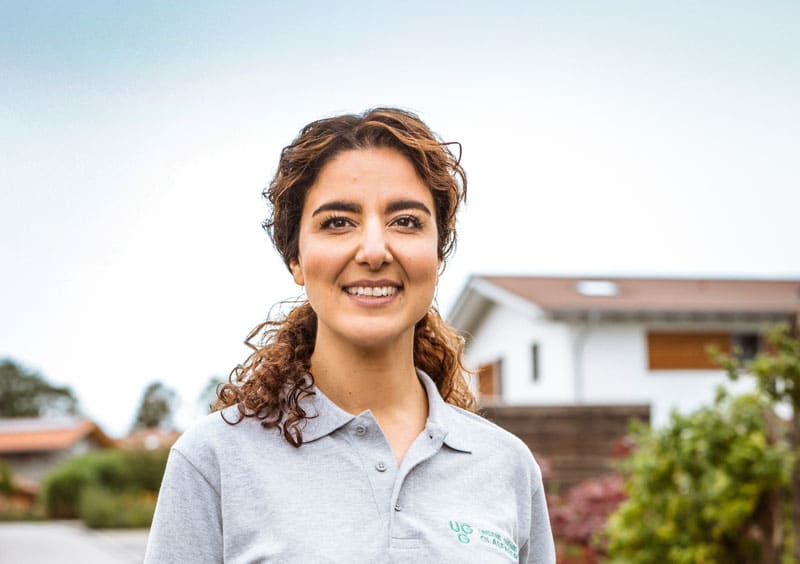 Mitarbeiterin von Unsere Grüne Glasfaser steht vor einem Wohnhaus und repräsentiert den Kundenservice für Glasfaserlösungen.