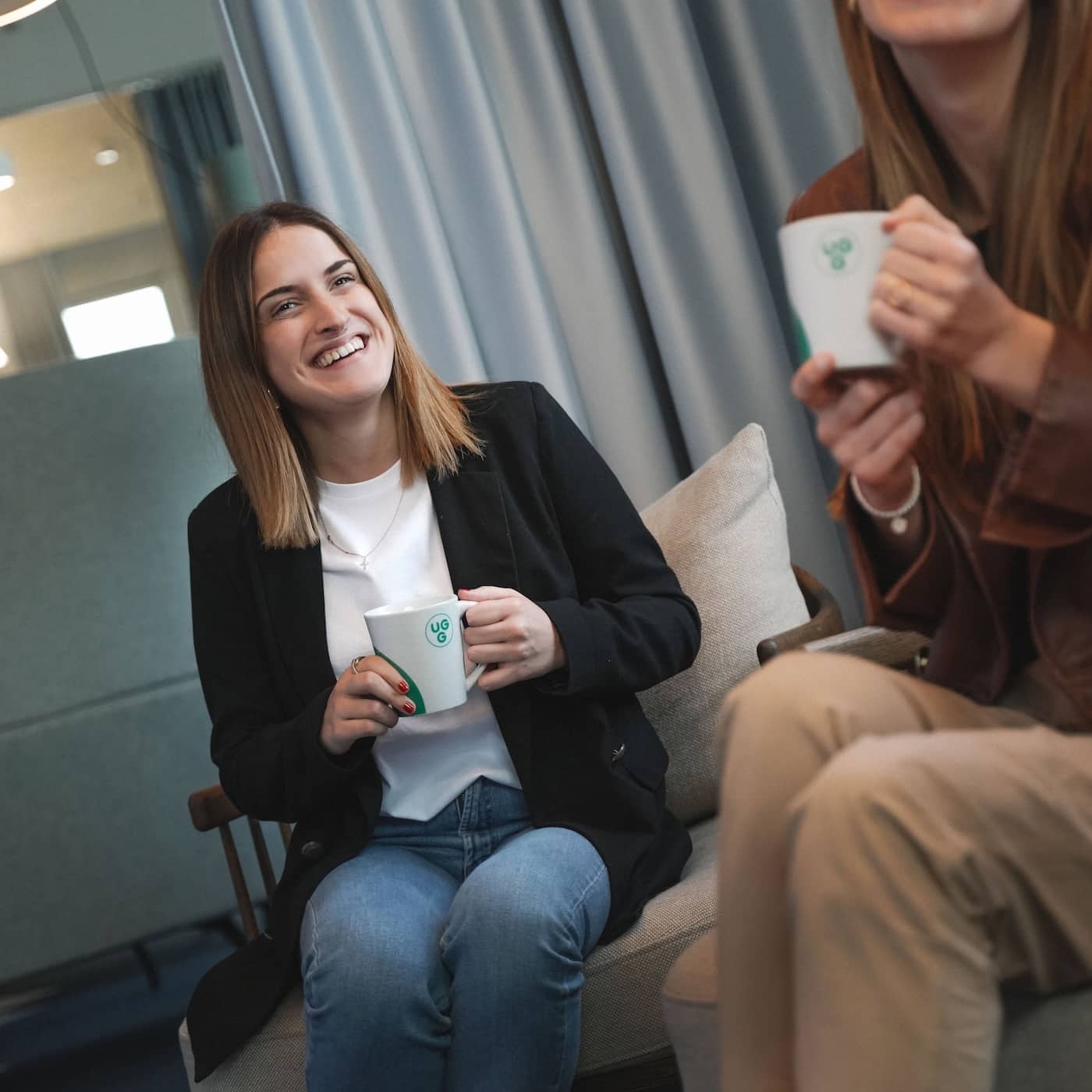Zwei Frauen genießen Kaffee in einem modernen Raum, symbolisieren die Gemeinschaft von Unsere Grüne Glasfaser.