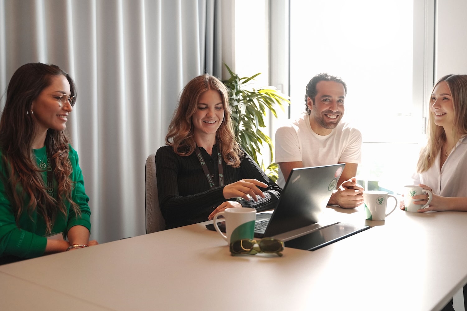 Teammeeting bei Unsere Grüne Glasfaser: Kreative Ideen und Zusammenarbeit in modernem Büro mit Laptop und Getränken.