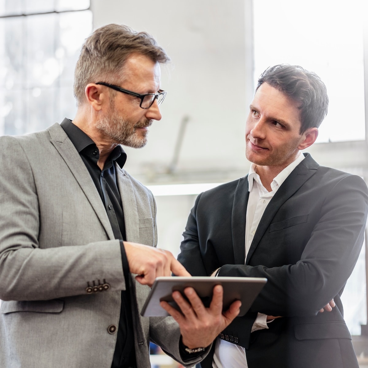 Zwei Geschäftsmänner diskutieren strategische Pläne mit einem Tablet in der Hand, ideal für digitale Lösungen von Unsere Grüne Glasfaser.