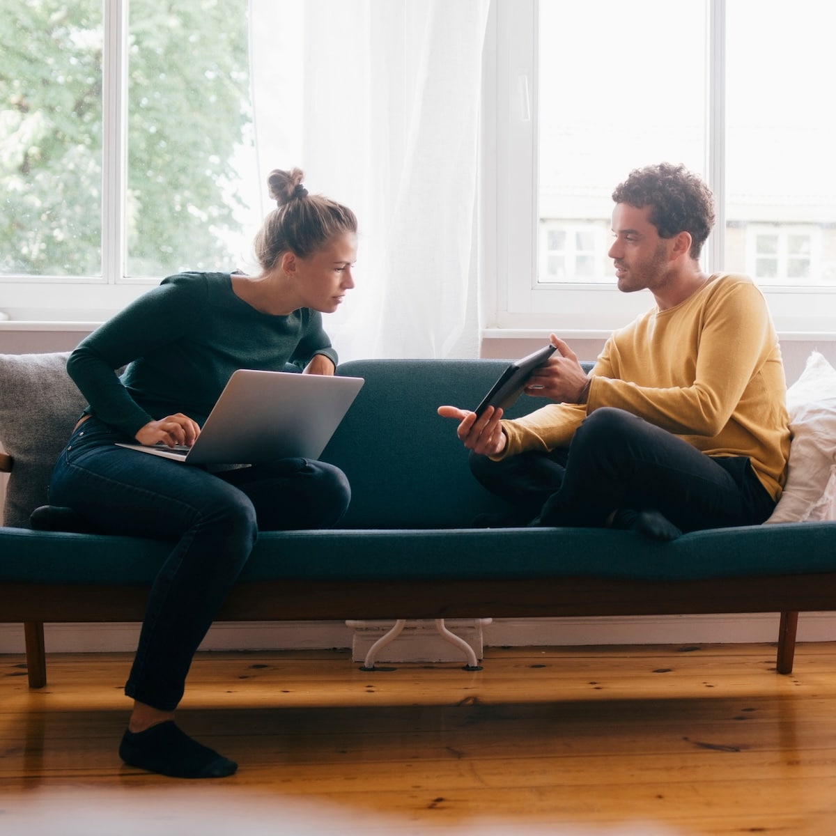 Zwei Personen diskutieren über digitale Geräte auf einem Sofa, symbolisieren moderne Kommunikation mit Glasfaserinternet.