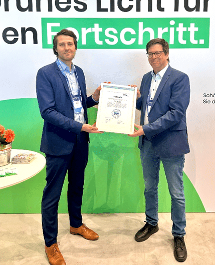 Zwei Männer überreichen sich eine Urkunde vor einem Banner von Unsere Grüne Glasfaser auf einer Messe.