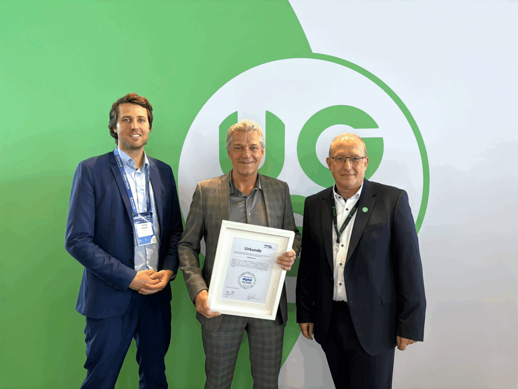 Vertreter von Unsere Grüne Glasfaser präsentieren stolz eine Auszeichnung auf einem Event mit grünem Hintergrund.