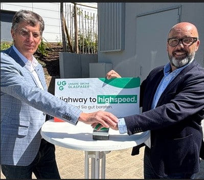 Zwei Männer aktivieren den Glasfaseranschluss von Unsere Grüne Glasfaser und präsentieren das Motto "Highway to Highspeed".