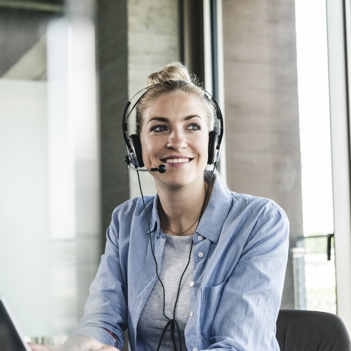 Kundensupport-Mitarbeiterin mit Headset bei "Unsere Grüne Glasfaser" im modernen Büro, freundlich lächelnd.